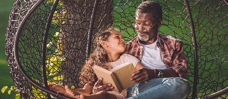 grandchild reading book while sitting in swinging hanging chair with grandfather